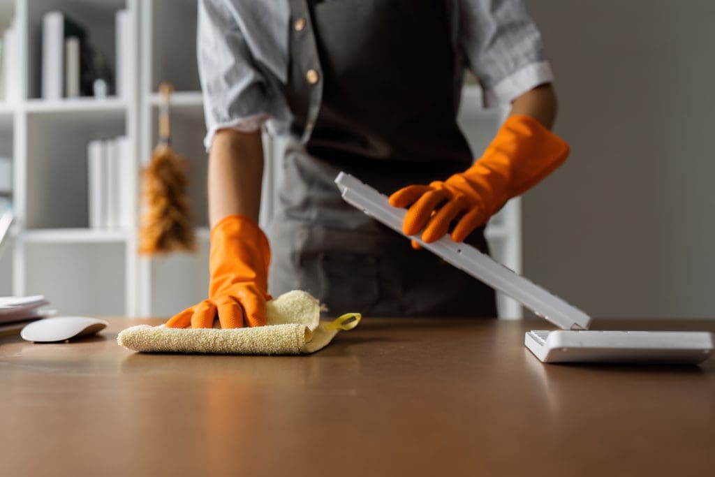A woman wearing orange gloves cleans an office as a part of a commercial cleaning service.